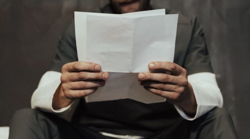 Mężczyzna trzyma w dłoniach rozłożone białe kartki papieru.
