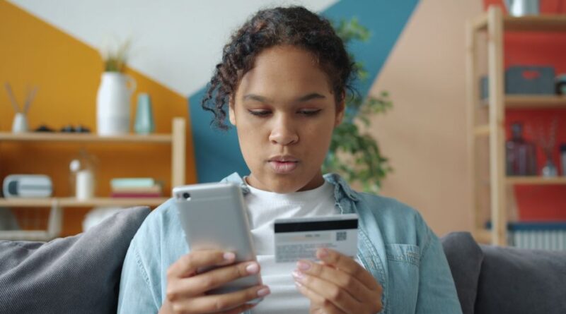 Młoda osoba trzymająca smartfon oraz kartę płatniczą.