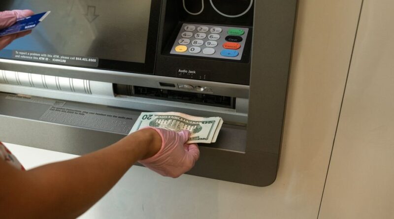 Ręka w różowej rękawiczce wkłada plik banknotów do szczeliny bankomatu.