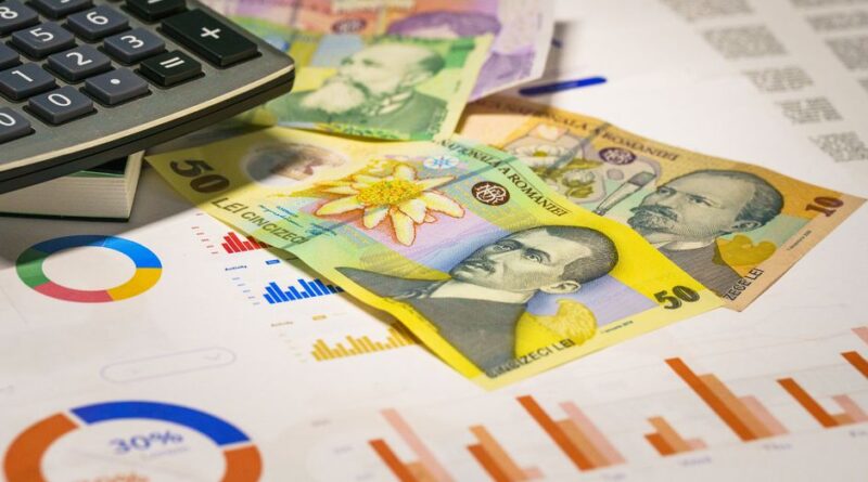 Banknoty i kalkulator leżące na kartce z kolorowymi wykresami finansowymi