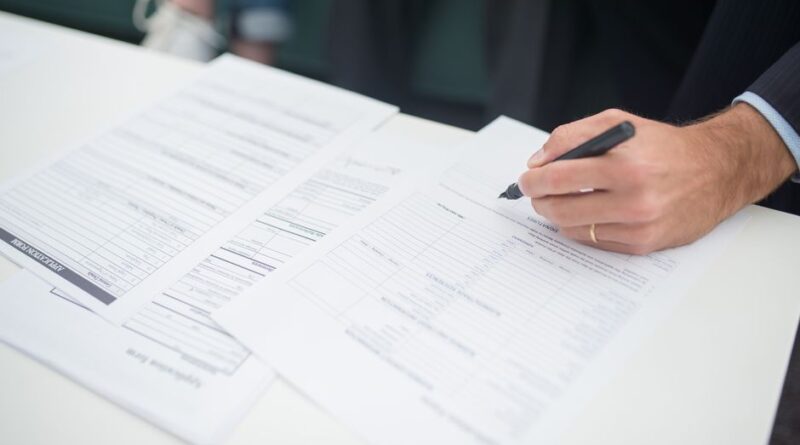 Mężczyzna podpisujący piórem formularz wniosku na białym biurku