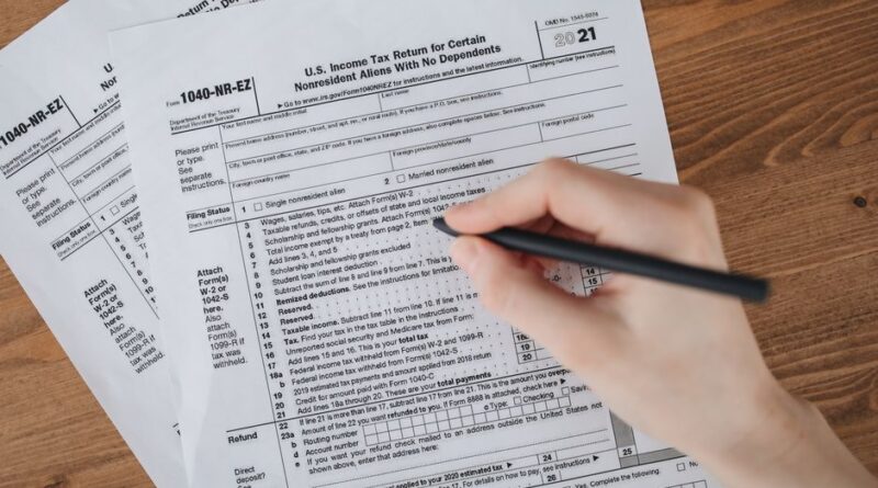 Ręka wypełniająca długopisem papierowy formularz podatkowy na drewnianym stole.
